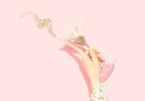 hand with sparkle tipping out of martini glass on pink background